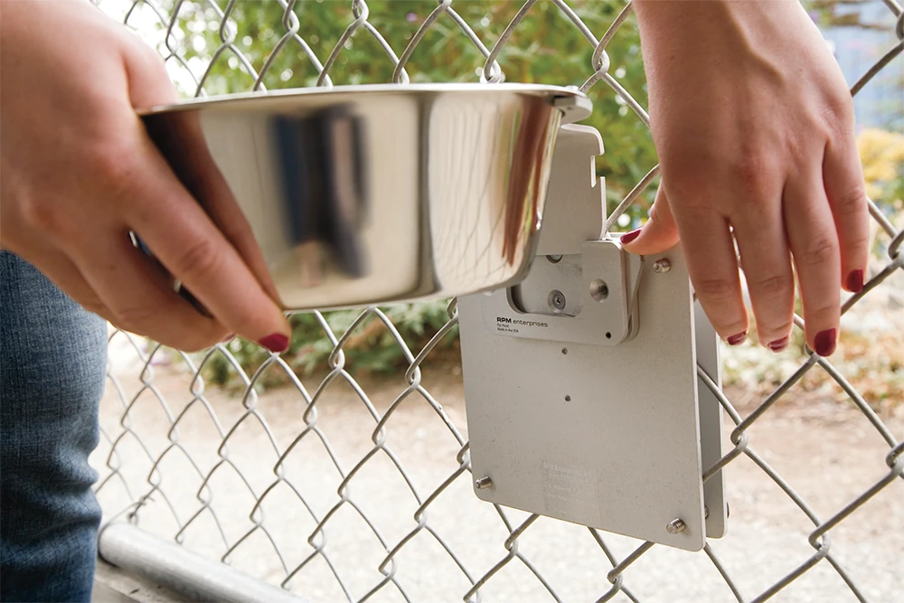 Hands attaching a Kennel Gear stainless bowl system to a kennel fence